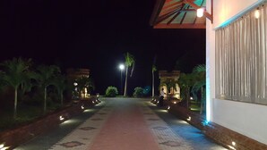Un sendero nocturno que conduce a un edificio con detalles arquitectónicos iluminados y palmeras.
