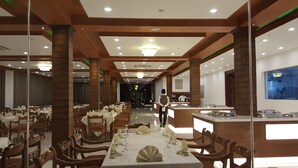 Un comedor amplio con varias mesas dispuestas para el servicio, una recepción y vistas del interior a través de un muro de cristal.