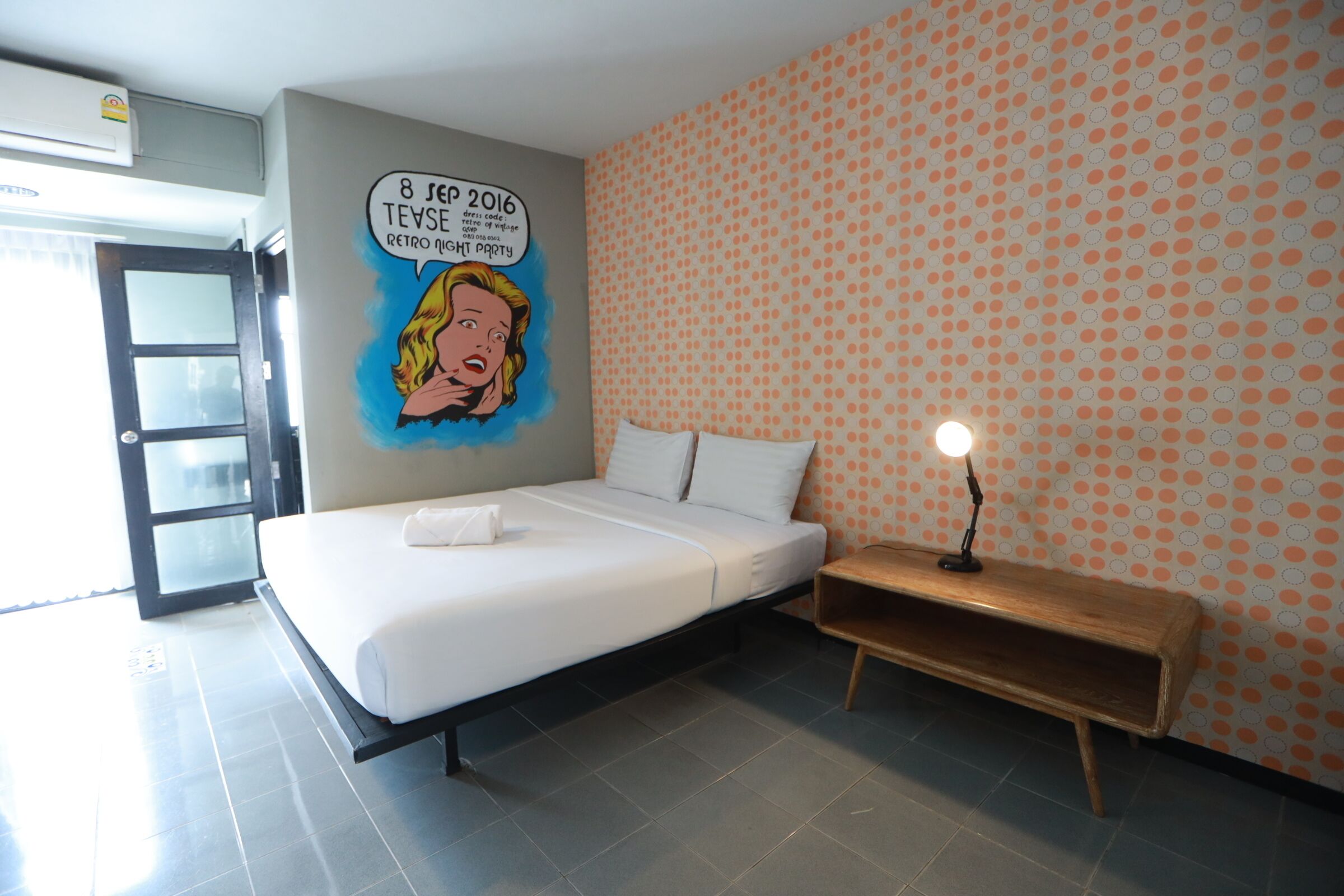 A modern hotel room with a bed, a nightstand, and a wall mural.