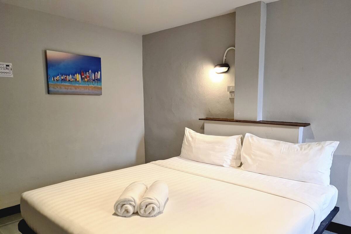 Une chambre d’hôtel avec un lit, des oreillers, un tableau au mur et un luminaire fixé au mur.