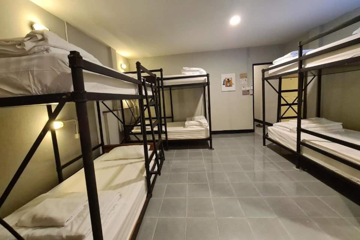 Une chambre de dortoir avec des lits superposés, un sol carrelé et un luminaire fixé au mur.