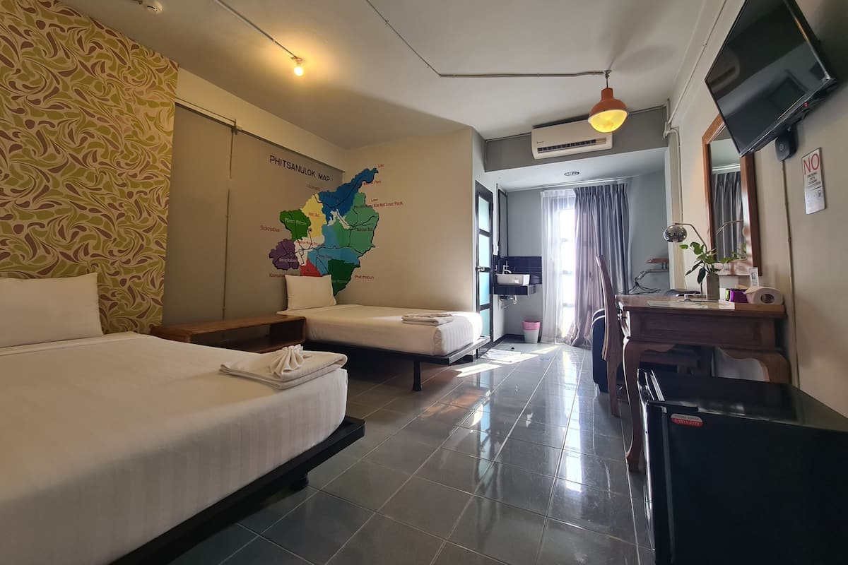 Une chambre d’hôtel avec un lit, un bureau, une chaise, une télévision, une carte accrochée au mur et une salle de bain visible à travers une porte ouverte.
