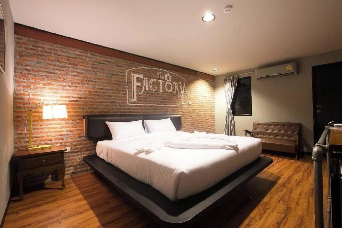 Une chambre d’hôtel avec un mur en briques, un lit, une table de chevet, une lampe, un canapé et un appareil de climatisation.