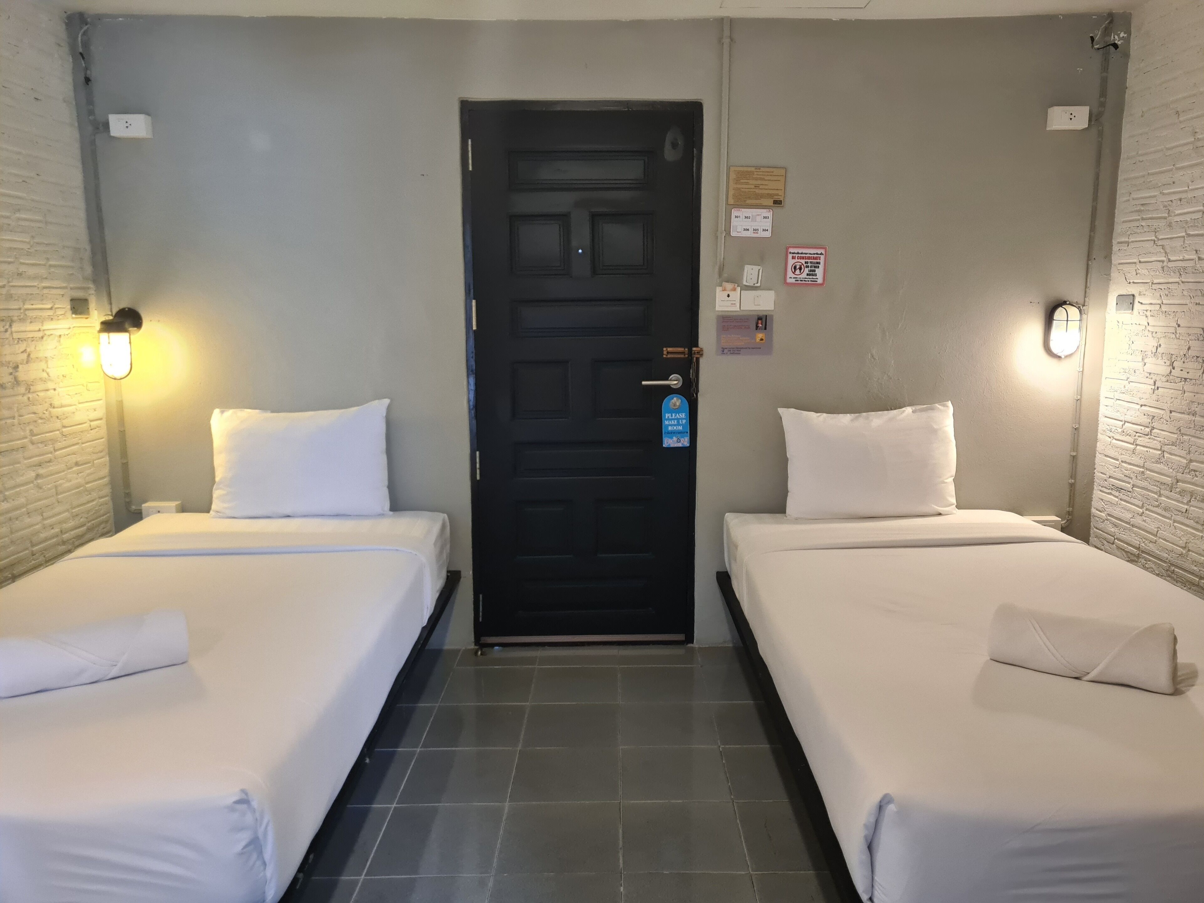 A hotel room with two single beds, a black door, and a light switch on the wall.