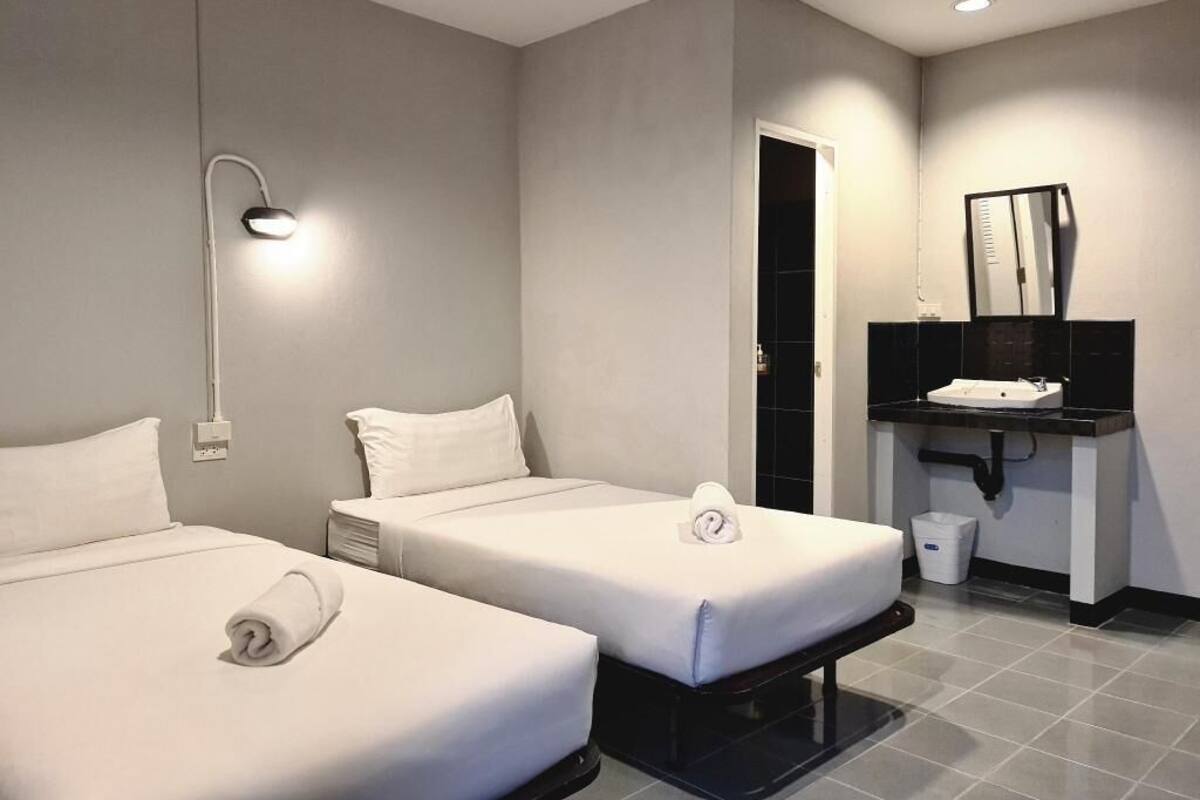 Une chambre d’hôtel avec deux lits, une salle de bain équipée d’un lavabo et d’un miroir, et une poubelle.