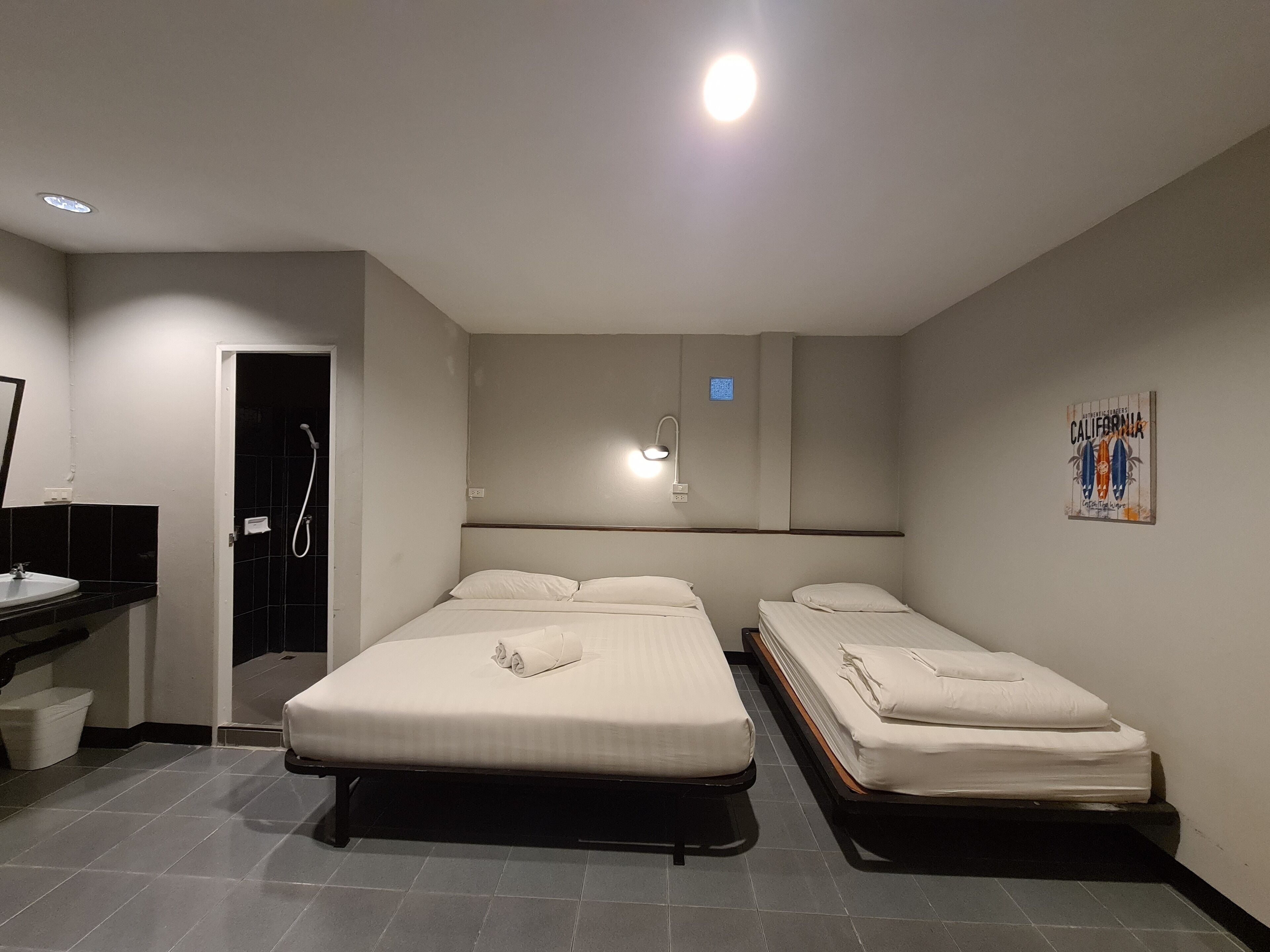 Habitación de hotel con dos camas individuales, un baño con ducha, lavamanos y un pequeño cubo de basura.