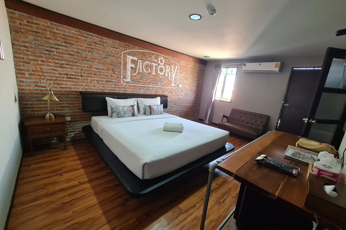 Une chambre d’hôtel avec un mur en briques, un lit avec du linge de maison blanc, un bureau en bois, une chaise et une petite table.