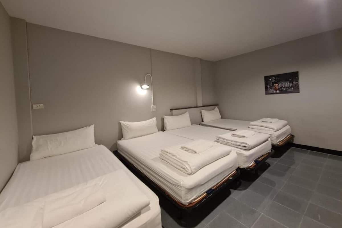 Une chambre d’hôtel avec trois lits, une veilleuse et une photographie représentant un paysage urbain accrochée au mur.