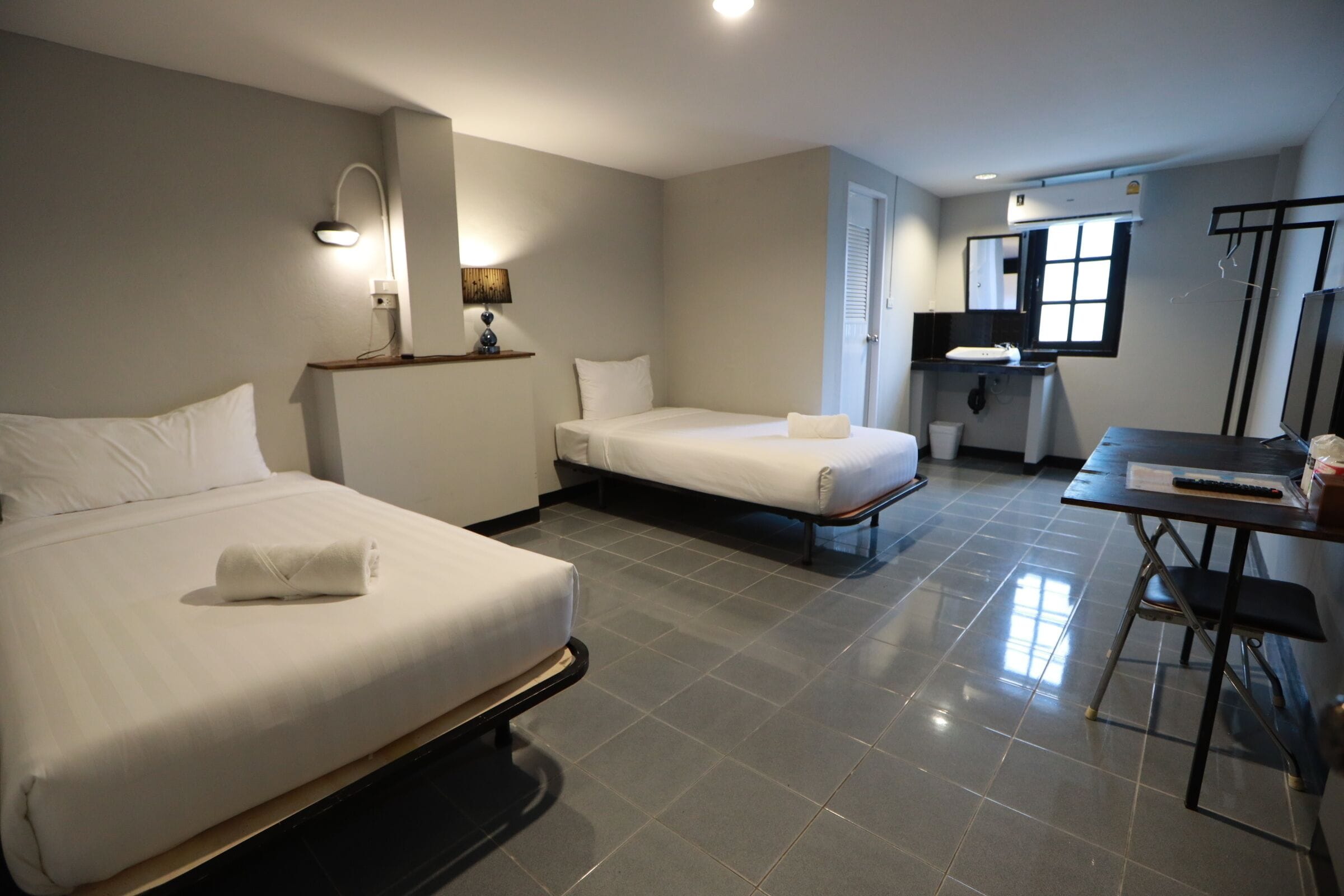 A hotel room with two beds, a desk, a mirror, and a window.