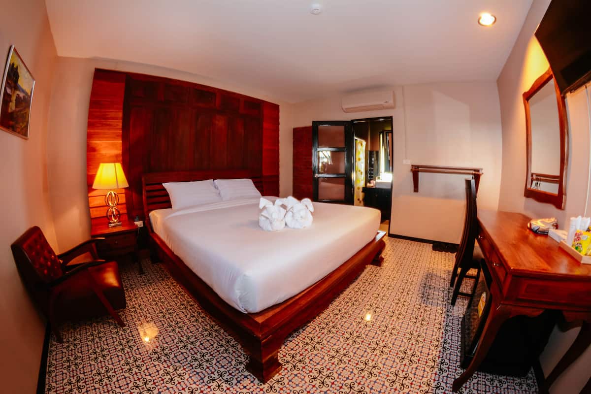 Une chambre d’hôtel avec un grand lit, une tête de lit en bois, un bureau avec une chaise, une lampe et un miroir.