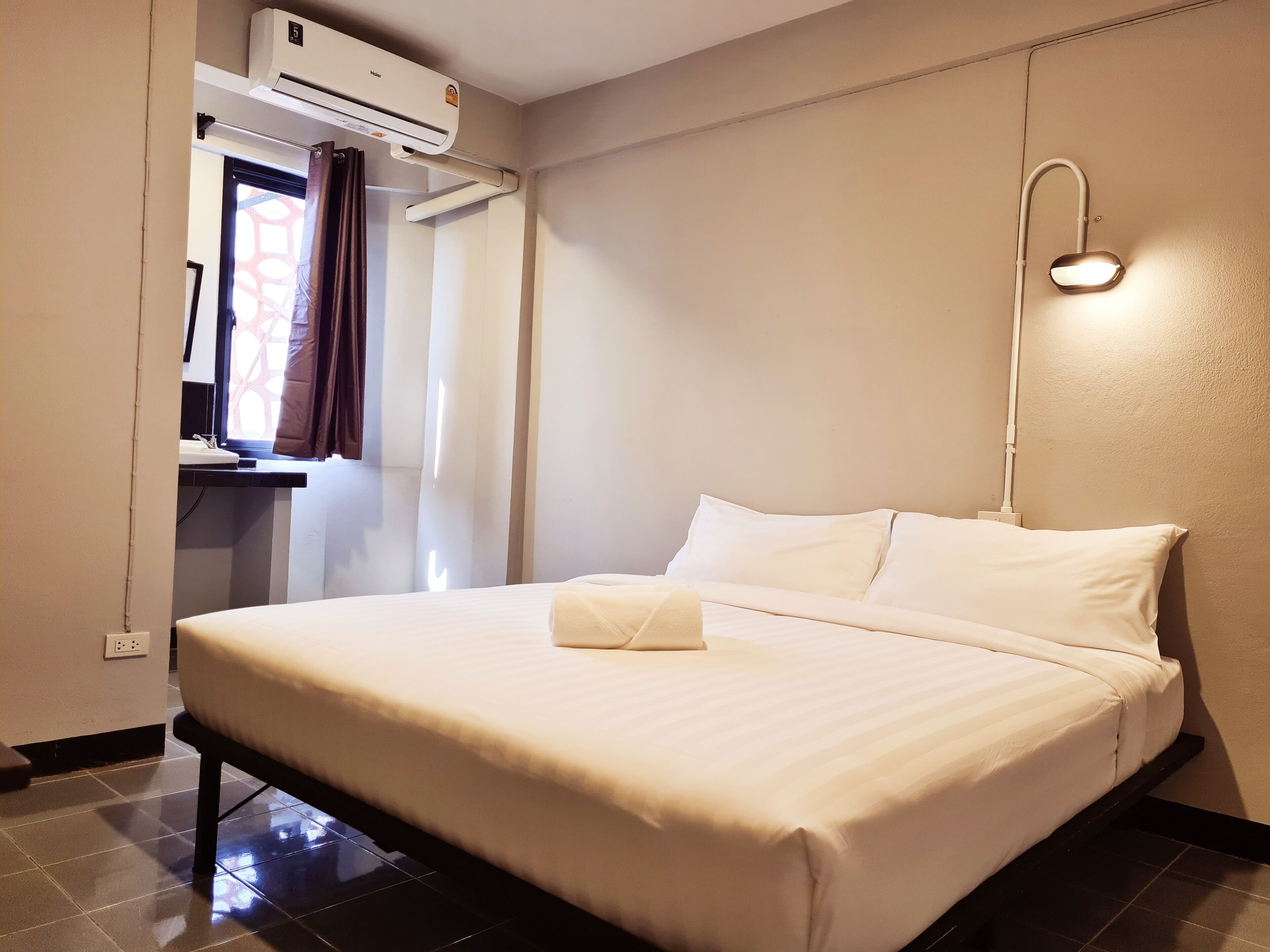 A neatly made bed with white linens, a bedside table with a lamp, and an air conditioning unit mounted on the wall.