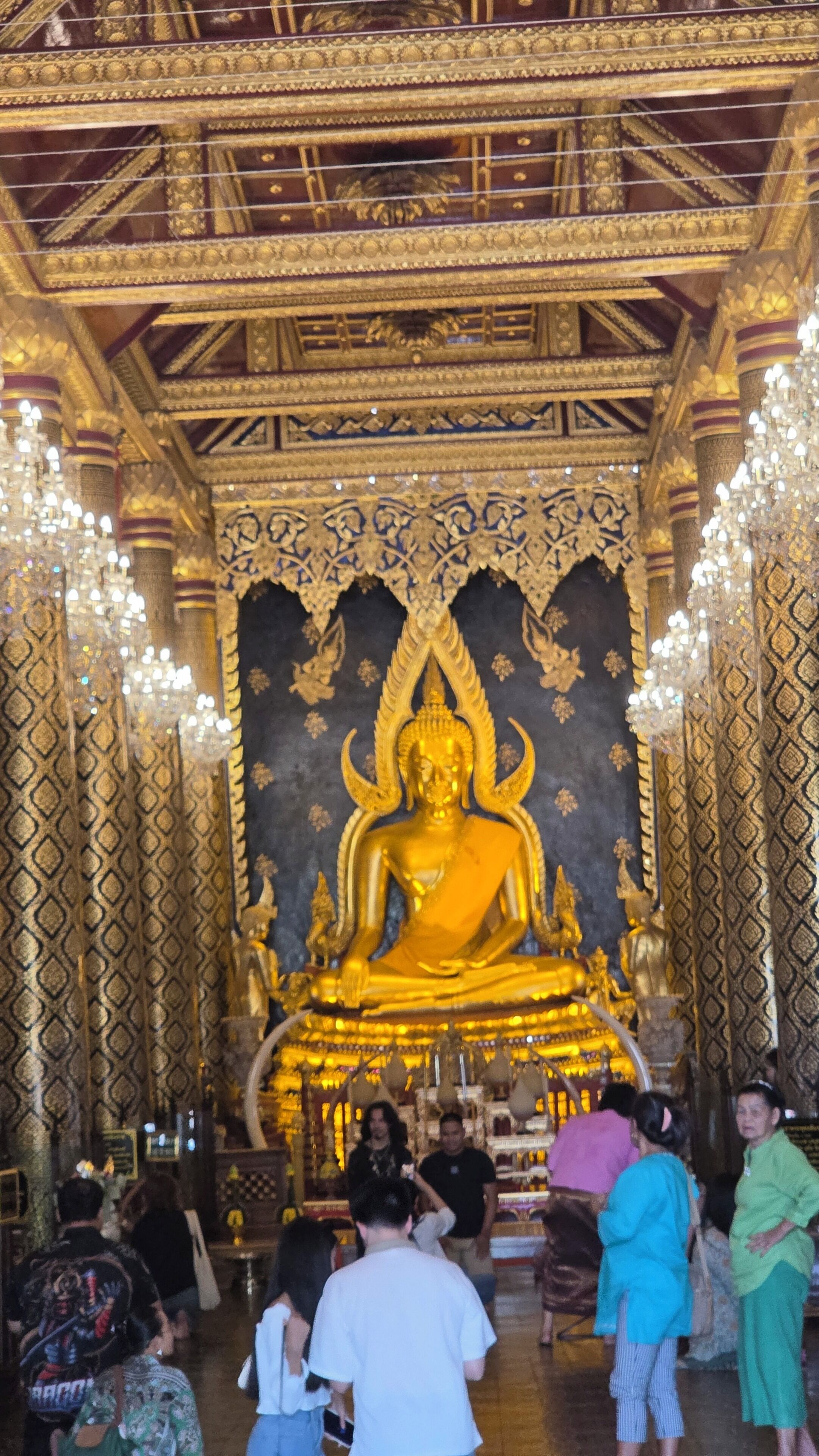 Eine große goldene Buddha-Statue in einem Tempel mit aufwendigen Mustern an Wänden und Decke.