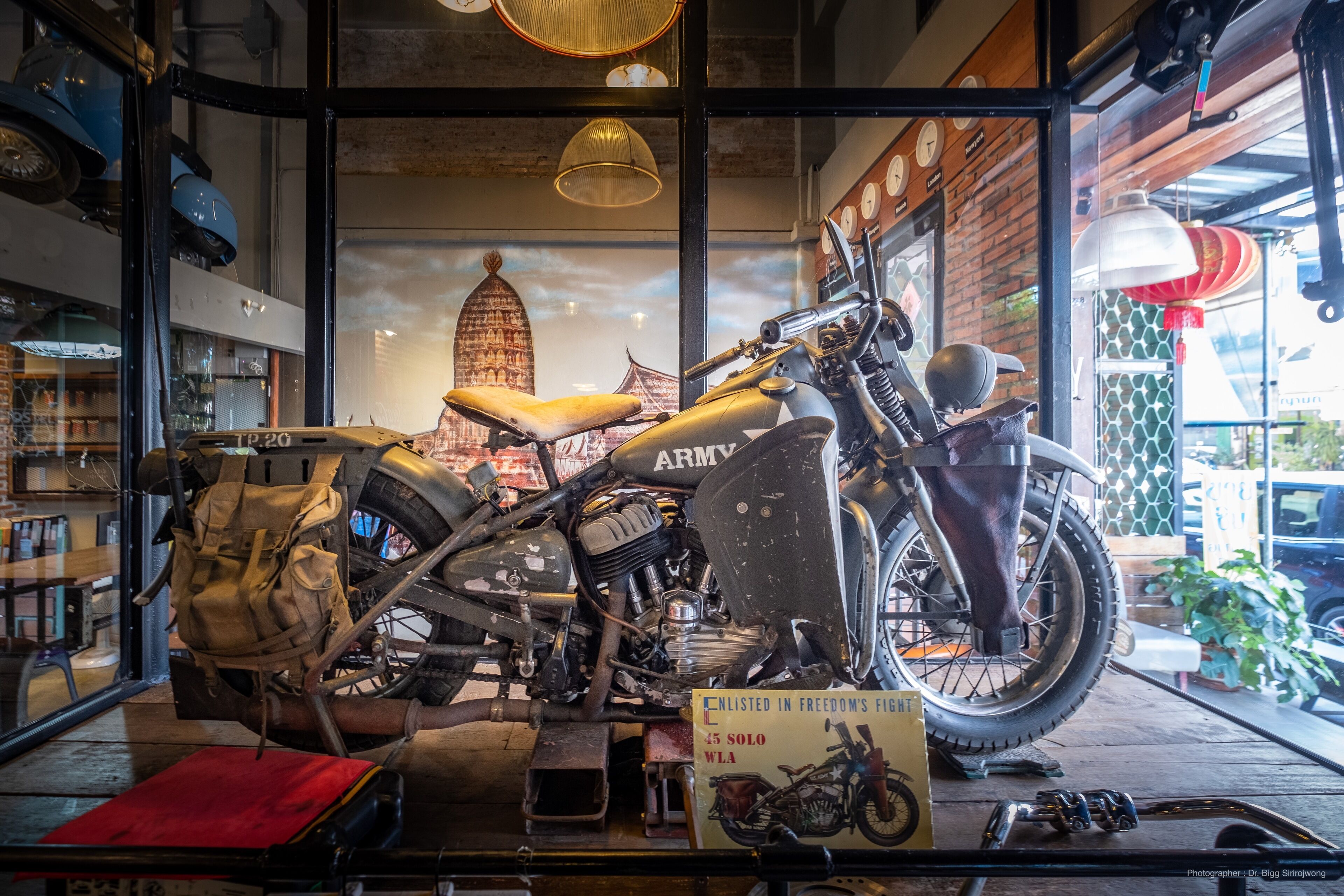 Une moto ancienne est exposée dans la vitrine d’un magasin, avec une pancarte indiquant qu’elle est présentée dans le catalogue « Freedom’s Fight ».