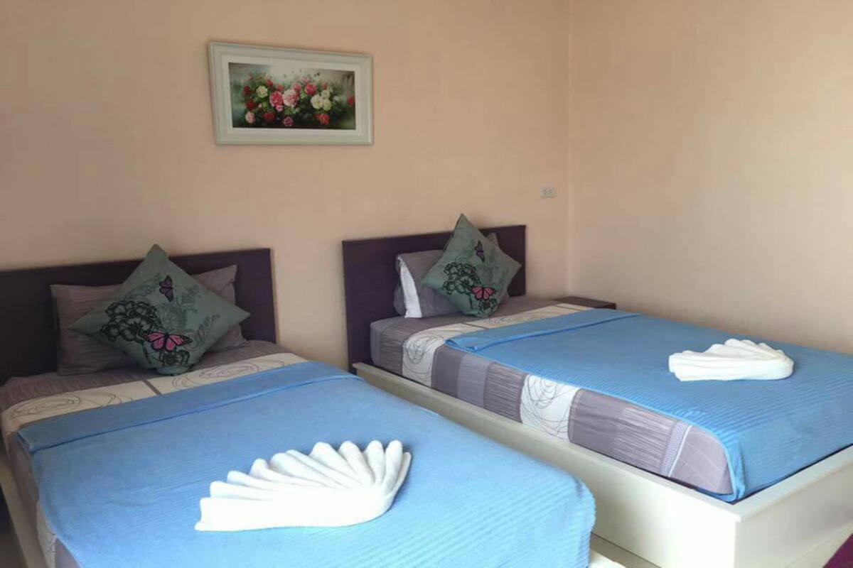 Two single beds with blue bedding and decorative pillows, a framed floral artwork on the wall, and a white towel folded on each bed.