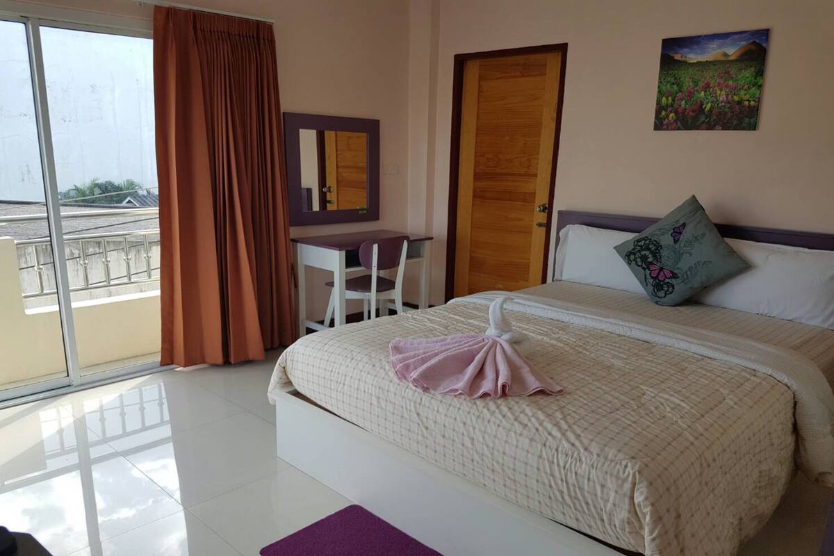 A hotel room with a bed, a desk, a chair, a large window with curtains, and a door.