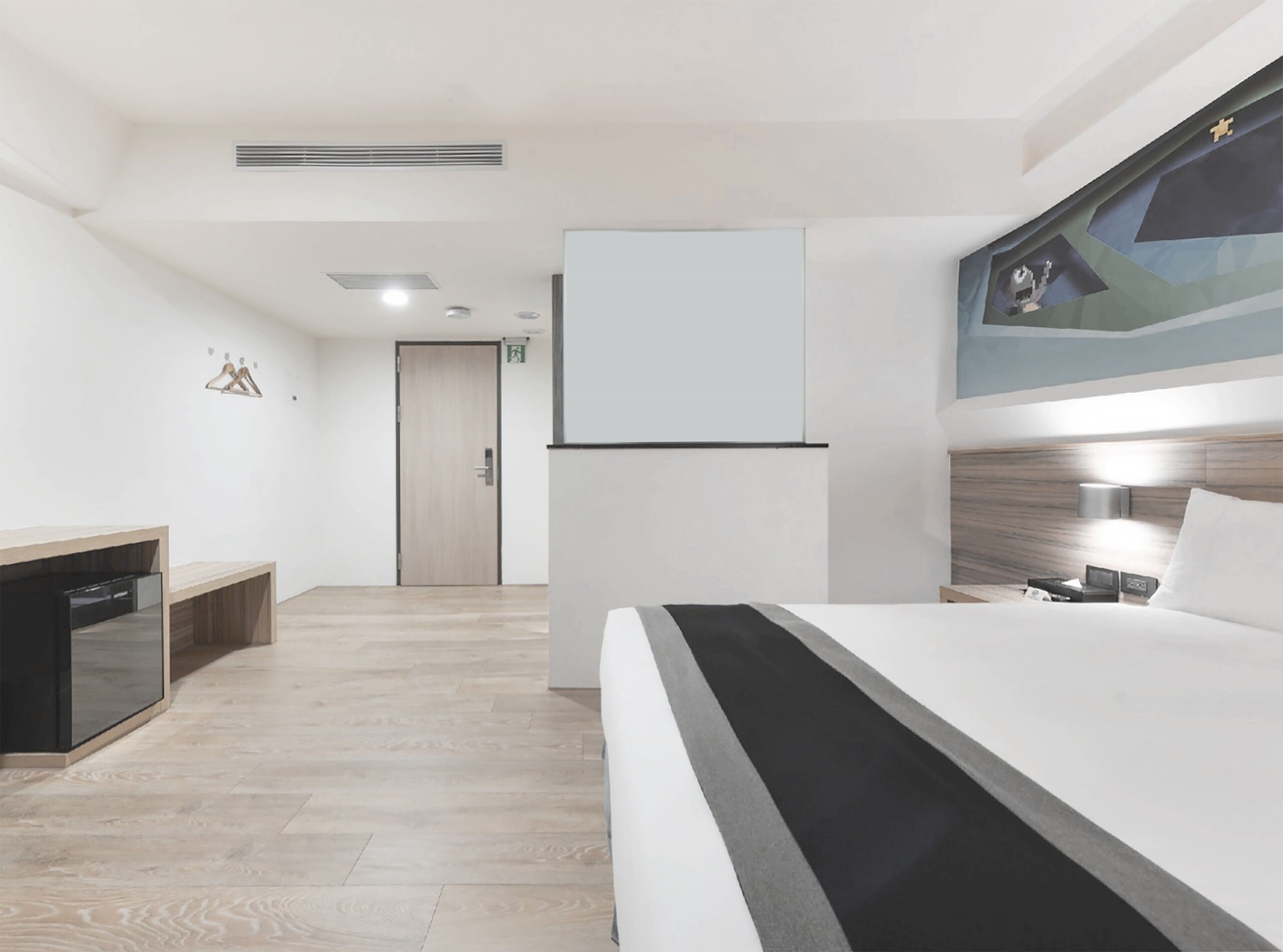 A modern hotel room with a bed, bedside table, lamp, and a painting on the wall.