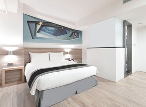Ein modernes Hotelzimmer mit Bett, Nachttischlampen, integriertem Fernseher und Kühlschrank.