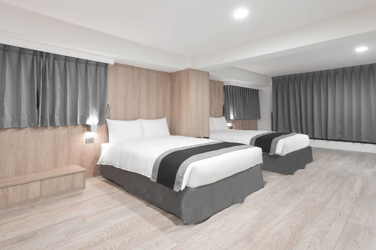 Una habitación de hotel moderna con dos camas, paneles de madera en las paredes y cortinas grises.