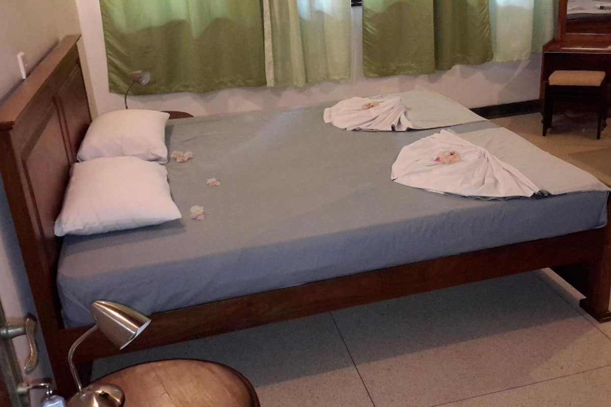 A neatly made bed with pillows and a blanket, a bedside table with a lamp, and a chair in a room with a window and curtains.