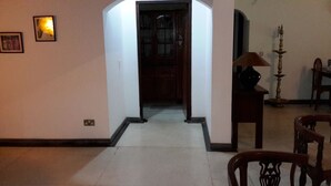 A hallway with a door leading to a dark room, a lamp on a table, and a chair in the foreground.