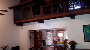 A dining area with wooden furniture, a staircase, and a colorful curtain.