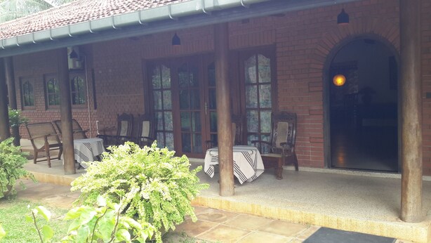A covered outdoor seating area with brick walls, large windows, and a door leading to an interior space.
