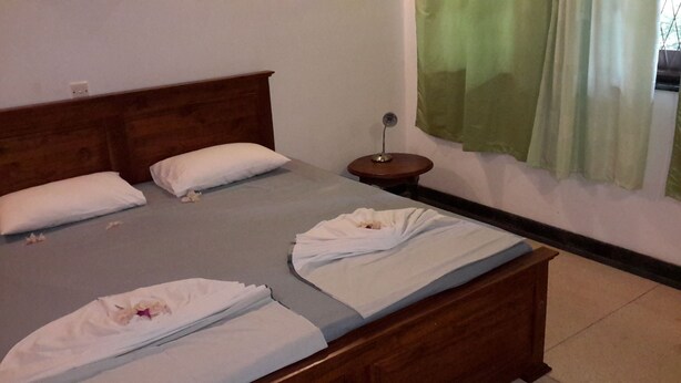 A bed with white linens, a wooden headboard, and a bedside table with a lamp. - Arangala Bungalow (Naula)
