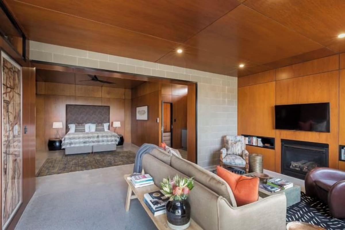 A hotel room with a bed, a sofa, a TV, a fireplace, and a bookshelf.