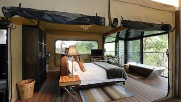 A tented room with a bed, a desk, a lamp, a television, and a view of the outdoors.