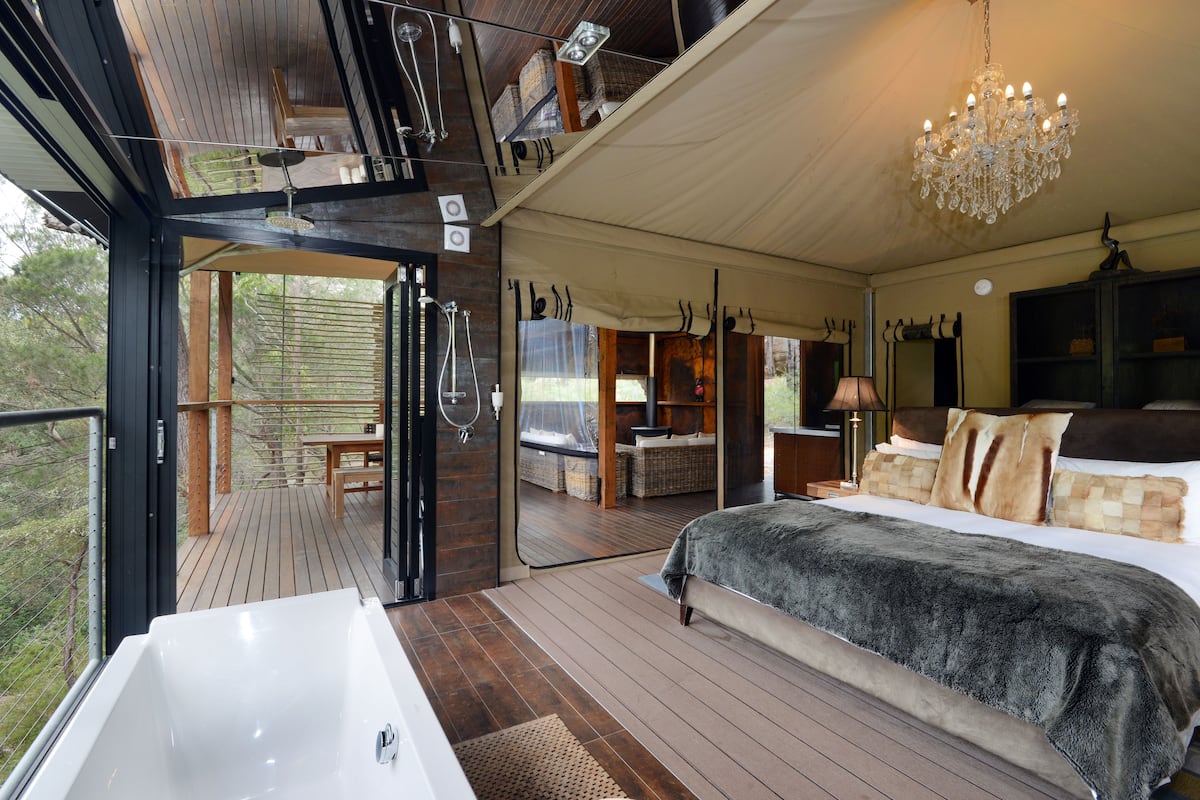 Une chambre spacieuse avec un grand lit, une baignoire et un balcon doté d’une terrasse en bois.