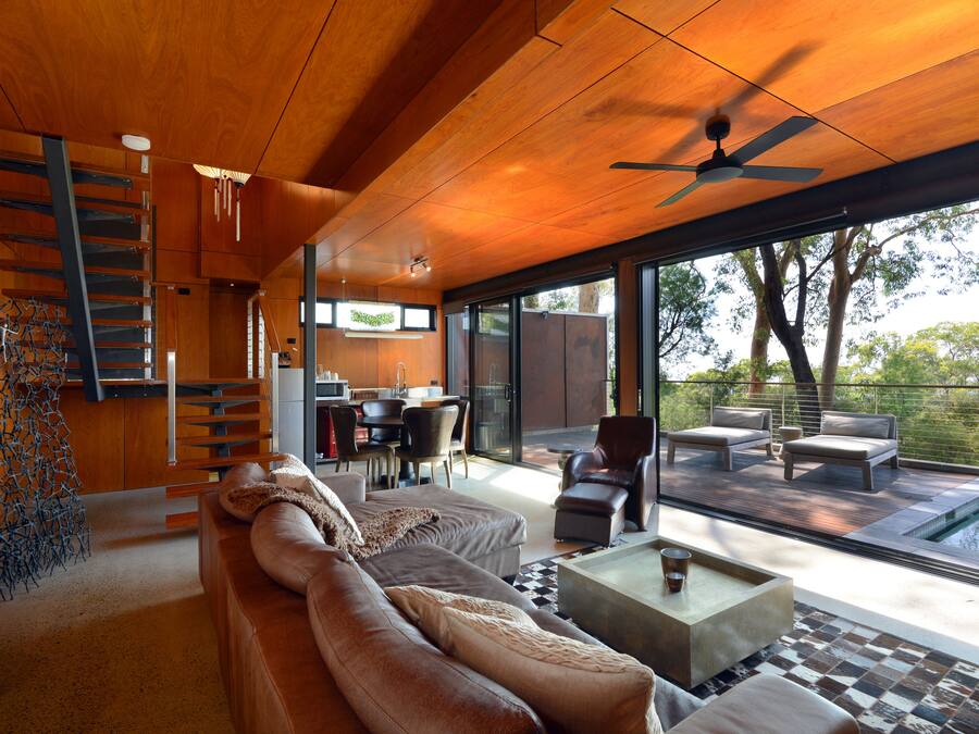 Un salon moderne avec un plafond en bois, un escalier, un coin repas et une vue sur une piscine.