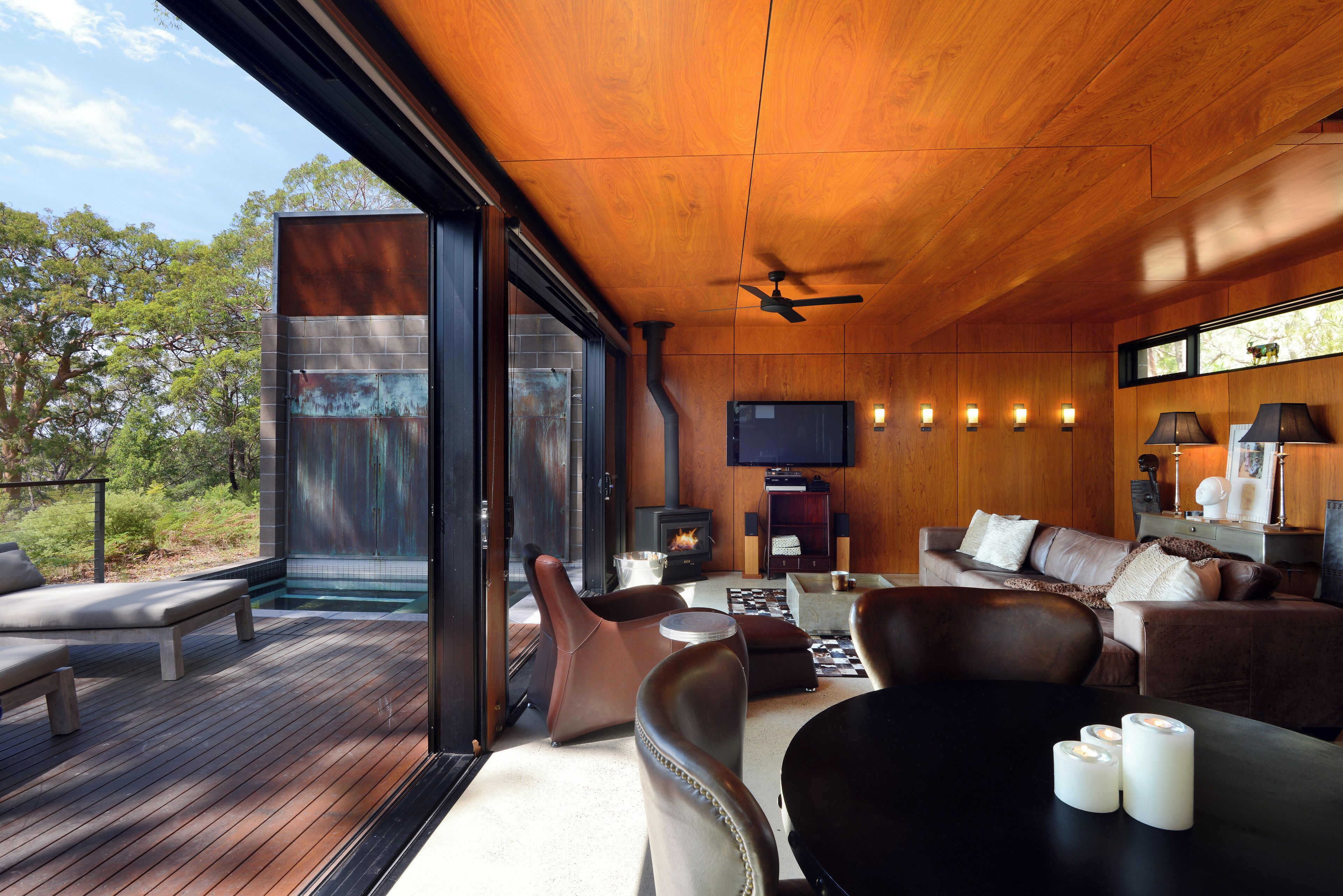 A modern living room with a wooden ceiling, a fireplace, and a large window overlooking a deck.
