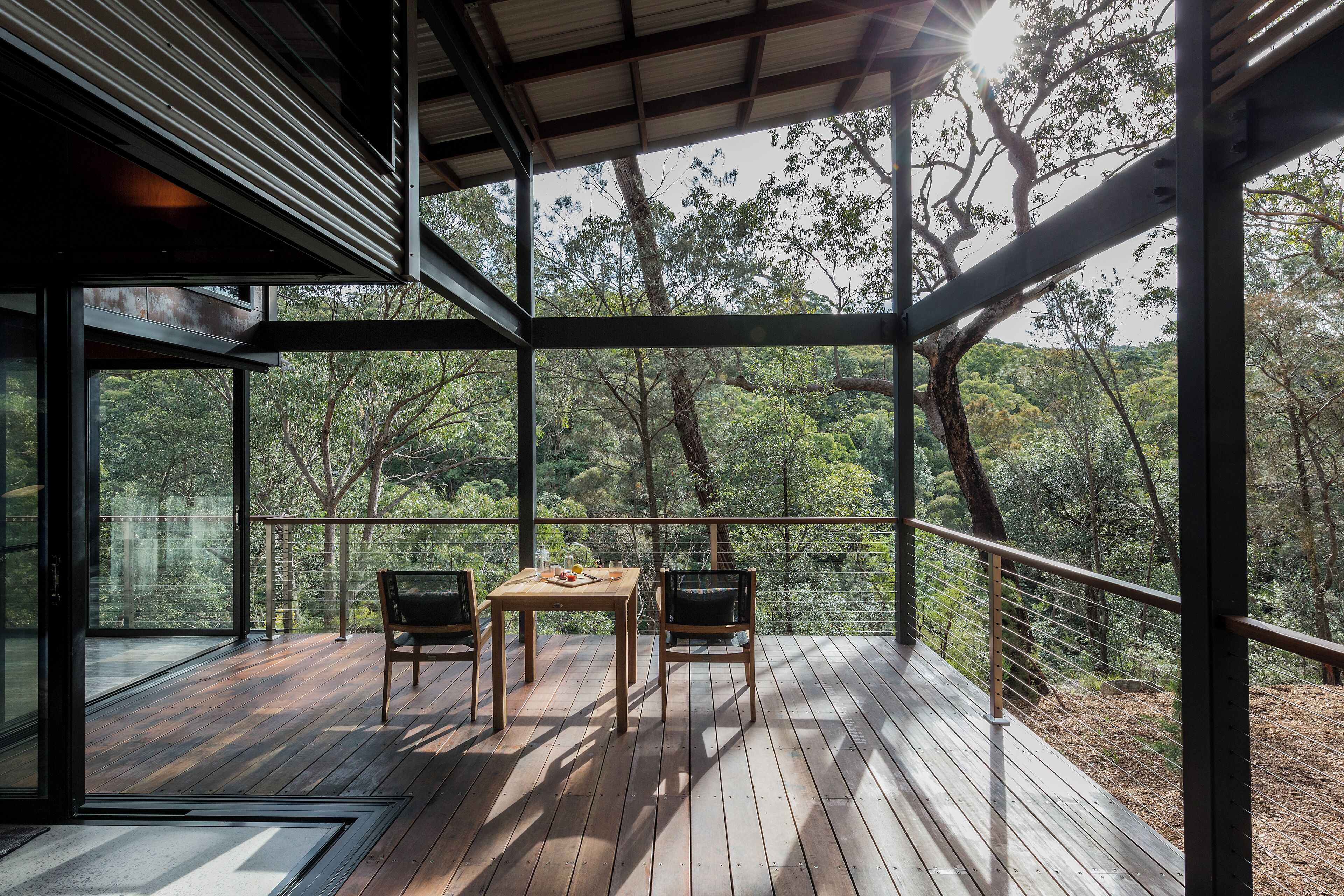 Terraza de madera con mesa y sillas, con vistas a un área boscosa.