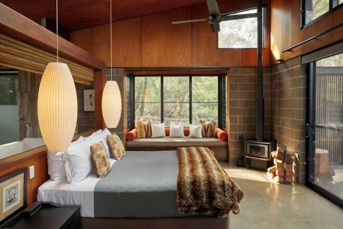 Une chambre dotée d’un grand lit, d’une banquette intégrée avec des coussins, d’une cheminée et de grandes fenêtres.