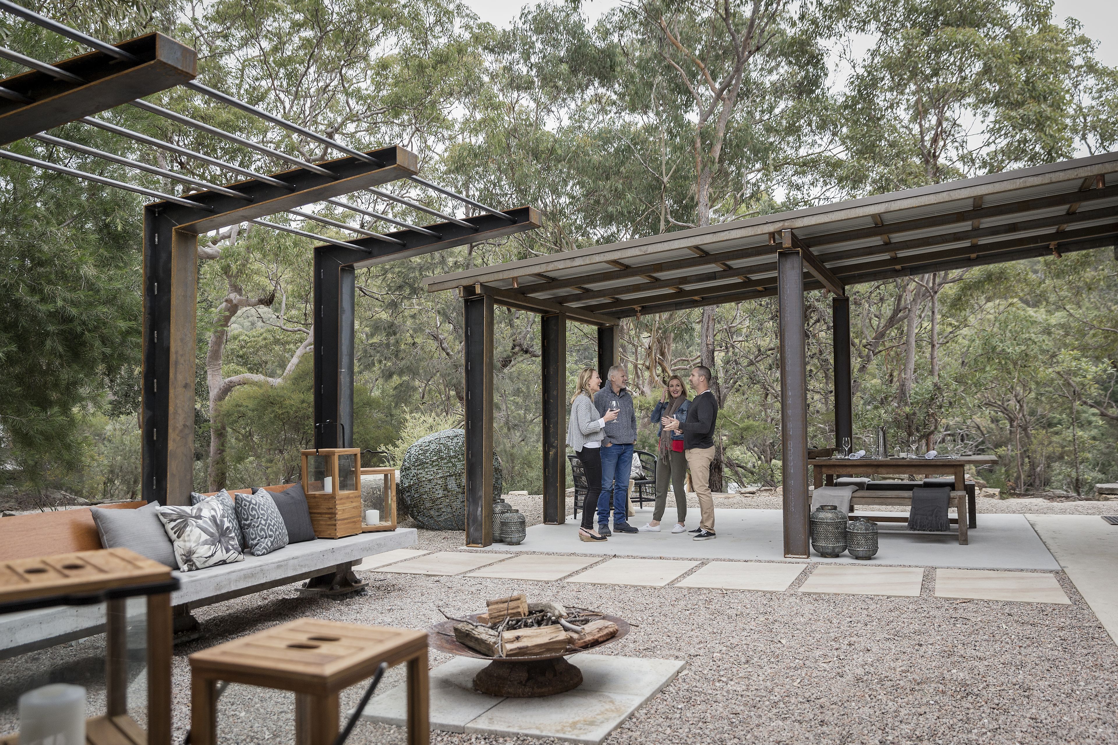 An outdoor patio with a wooden bench, a fire pit, and a pergola structure.