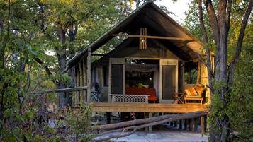 Relax on the elevated deck with a bench and table, surrounded by a tranquil forest setting.