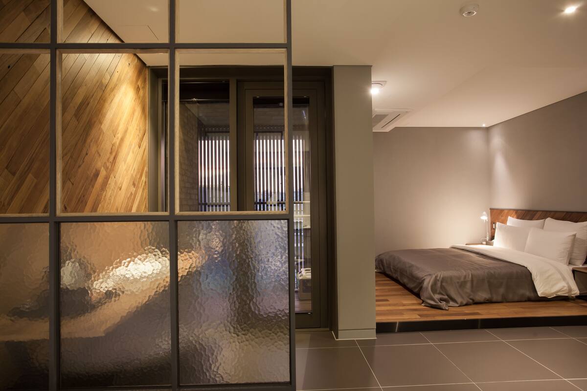 Une chambre moderne avec un grand lit, une table de chevet et une vue sur un balcon grâce à une cloison en verre.