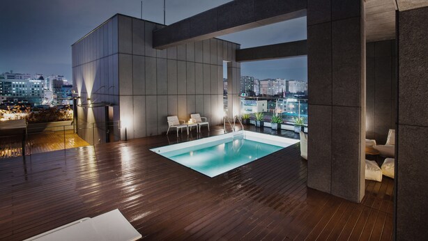 A rooftop pool area with a view of the city skyline, modern architecture, and seating by the pool. - Hotel Gaden by Onyu stay (Suwon)