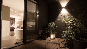 A modern outdoor area with a wooden deck, a glass door leading to a room with a bathtub, and potted plants. - Hotel Gaden by Onyu stay (Suwon)