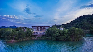 A modern two-story house with a balcony, surrounded by dense greenery and a body of water. - Fishman homestay (Hangzhou)