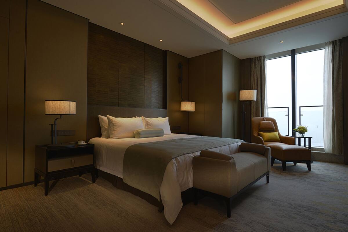 A hotel room with a large bed, bedside lamps, a chair, and a view of the outdoors.