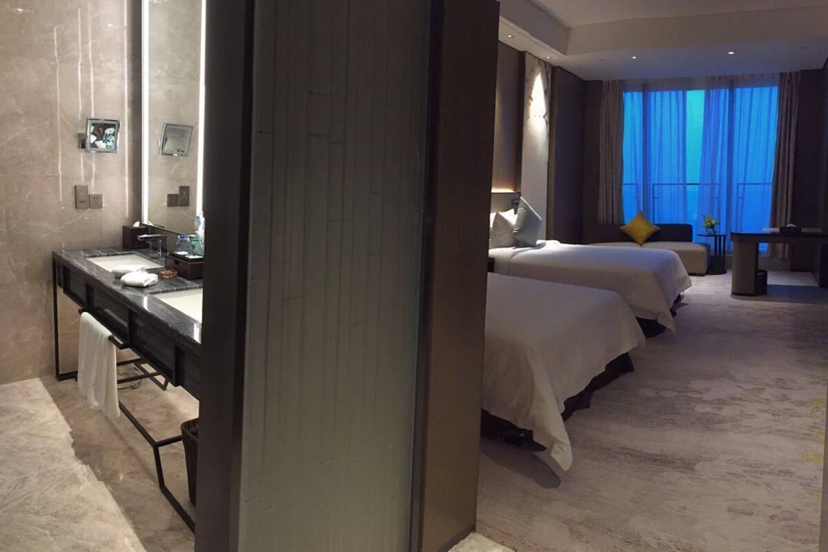 A hotel room with a large bed, a desk, and a bathroom with a mirror and sink.