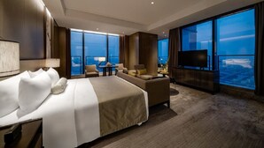 Habitación de hotel moderna con una cama grande, un sofá, un televisor y un balcón con vistas a la ciudad.