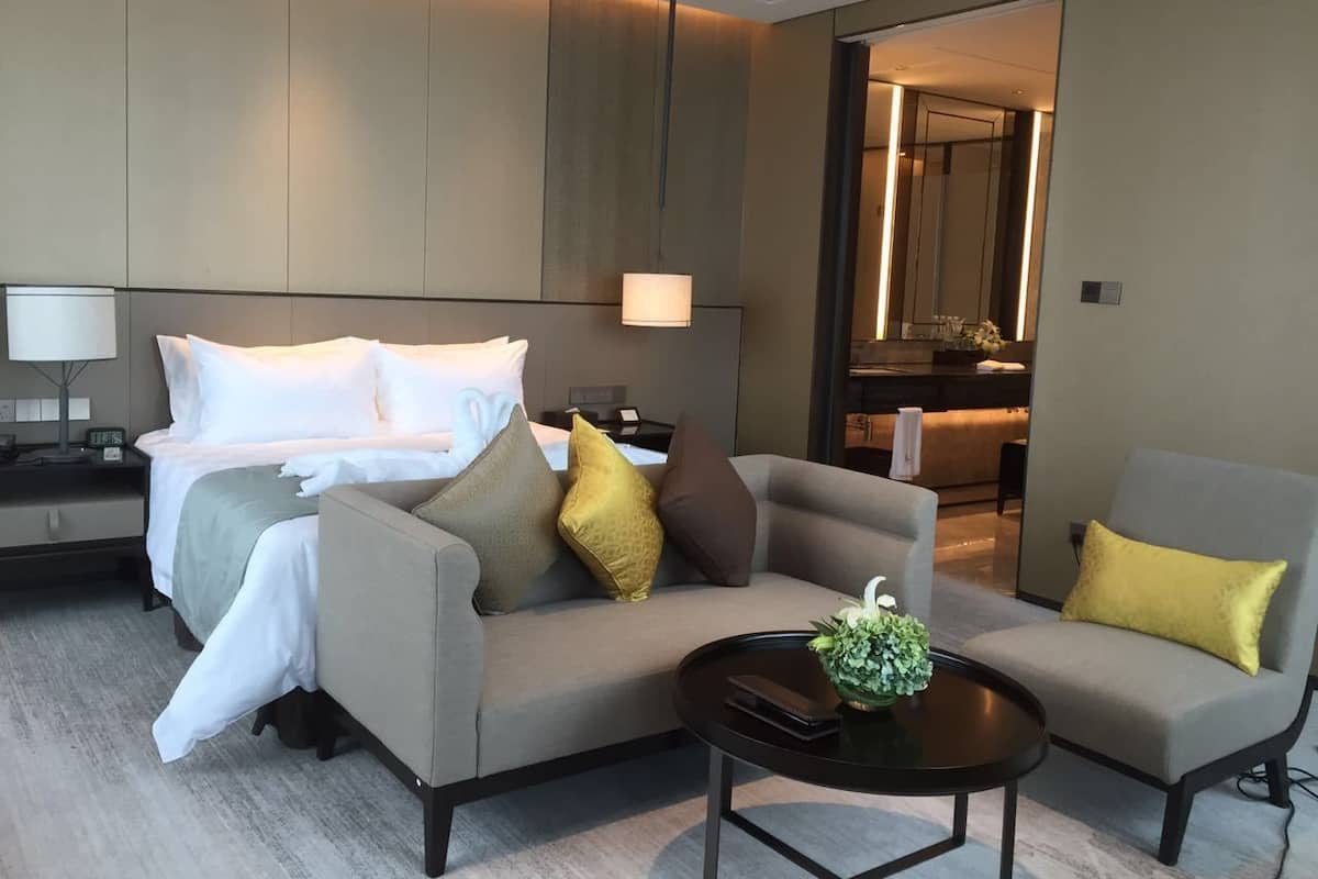 A modern hotel room with a bed, two sofas, a coffee table, and a desk with a lamp.