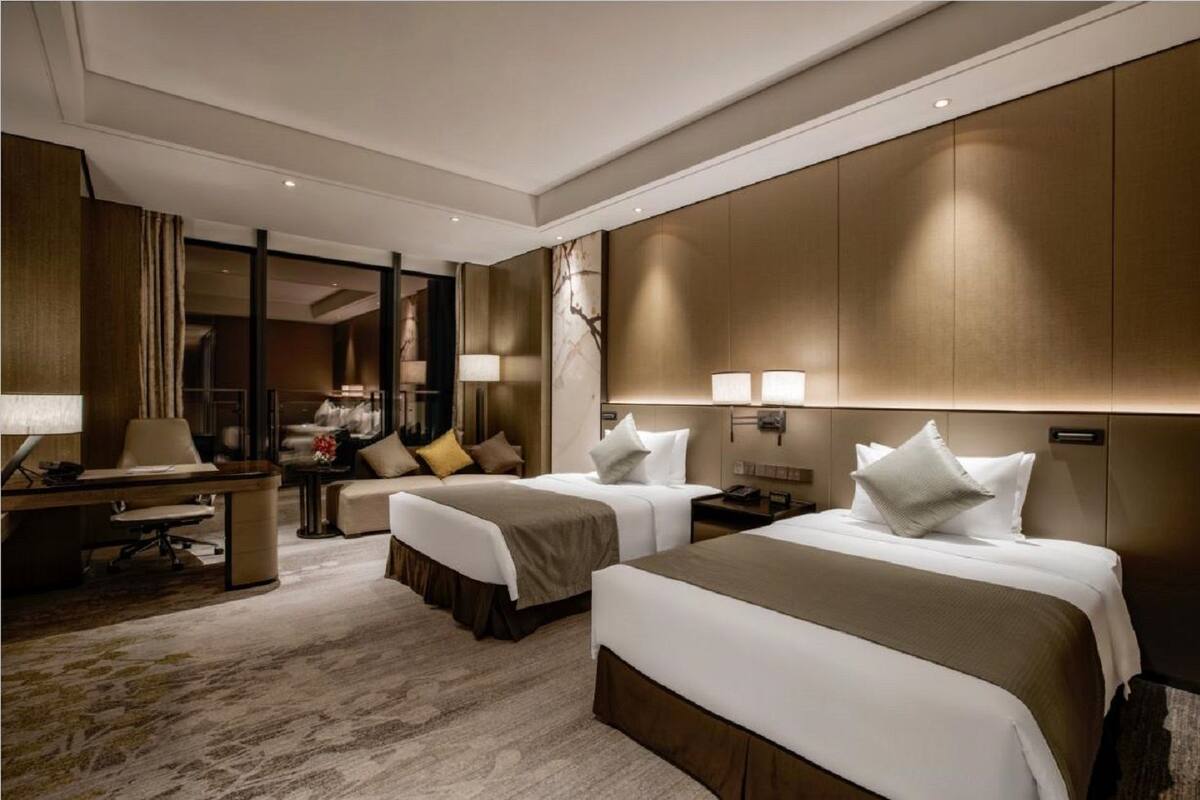 A hotel room with two beds, a desk, a chair, and a large mirror.