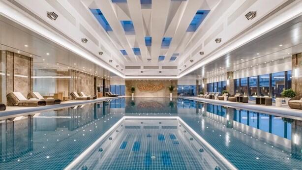 Una amplia piscina interior con zonas de descanso a ambos lados, un diseño de techo moderno y una pared decorativa central.