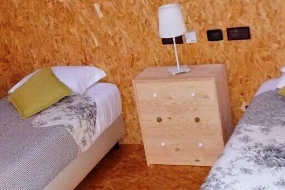 A small, cozy room with two beds, each with a pillow and a lamp on a wooden nightstand.
