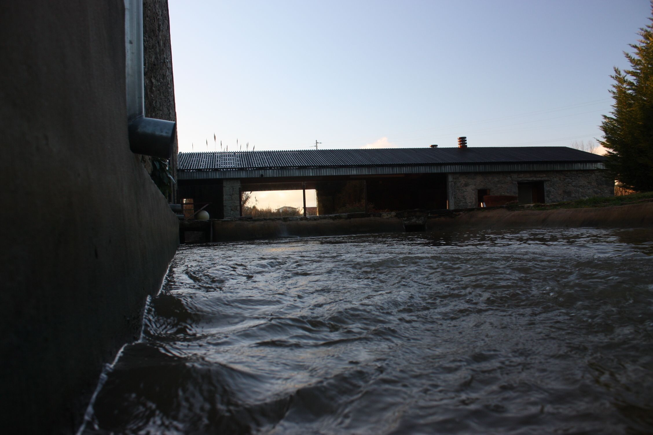 Een rivier stroomt langs een stenen gebouw met een metalen dak.