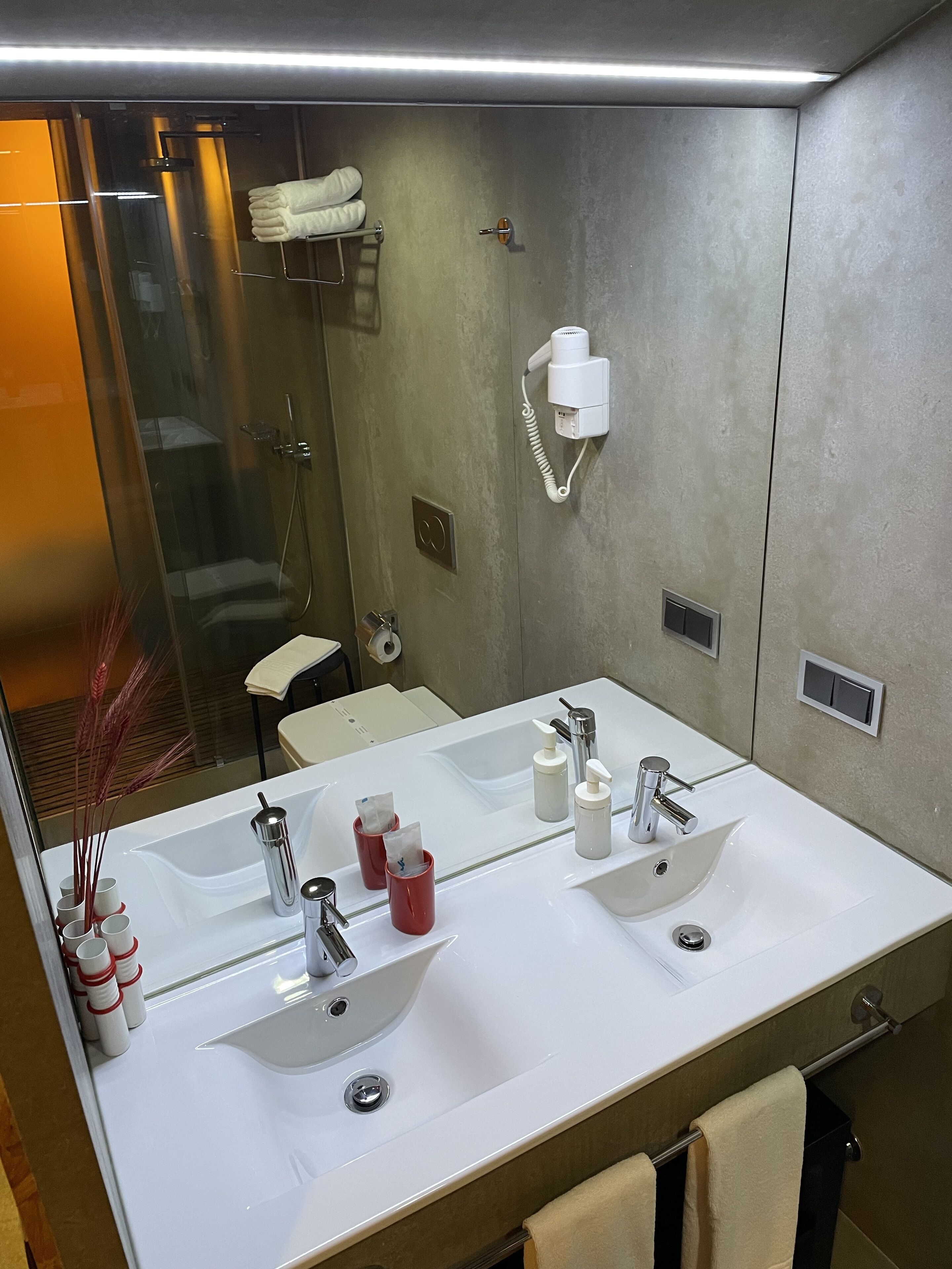 A modern bathroom with two sinks, a large mirror, and a hairdryer mounted on the wall.