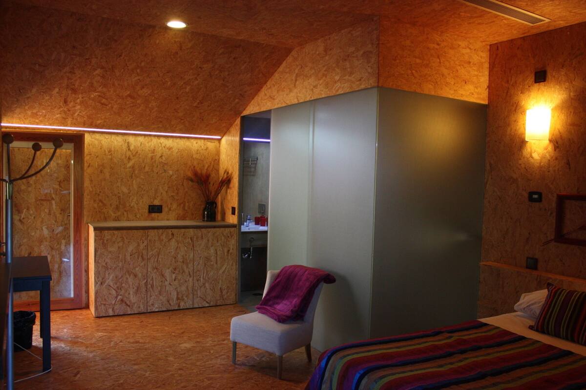 A bedroom with a bed, a chair, a desk, and a kitchenette.